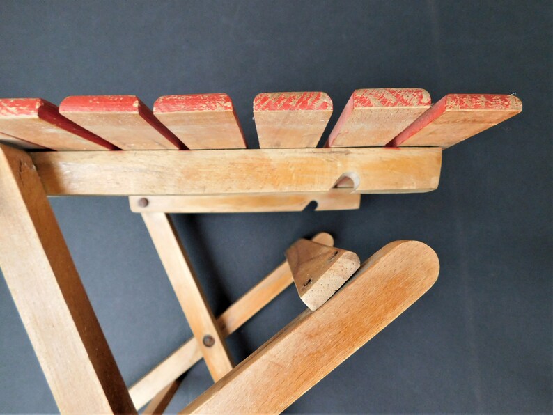 May include: A wooden folding chair with red painted slats on the back. The chair is made of natural wood and has a simple design.