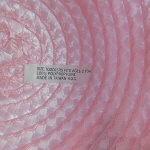 May include: Pink toddler hat made of 100% polypropylene. The hat has a label that reads "Size: Toddlers Fits Ages 2 to 4, 100% Polypropylene, Made in Taiwan R.O.C."