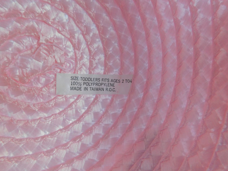 May include: Pink toddler hat made of 100% polypropylene. The hat has a label that reads "Size: Toddlers Fits Ages 2 to 4, 100% Polypropylene, Made in Taiwan R.O.C."