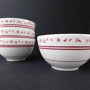 May include: White ceramic bowls with a red floral and stripe design. The bowls are stacked in a group of three and a single bowl is next to them. The bowls have a classic, vintage aesthetic.