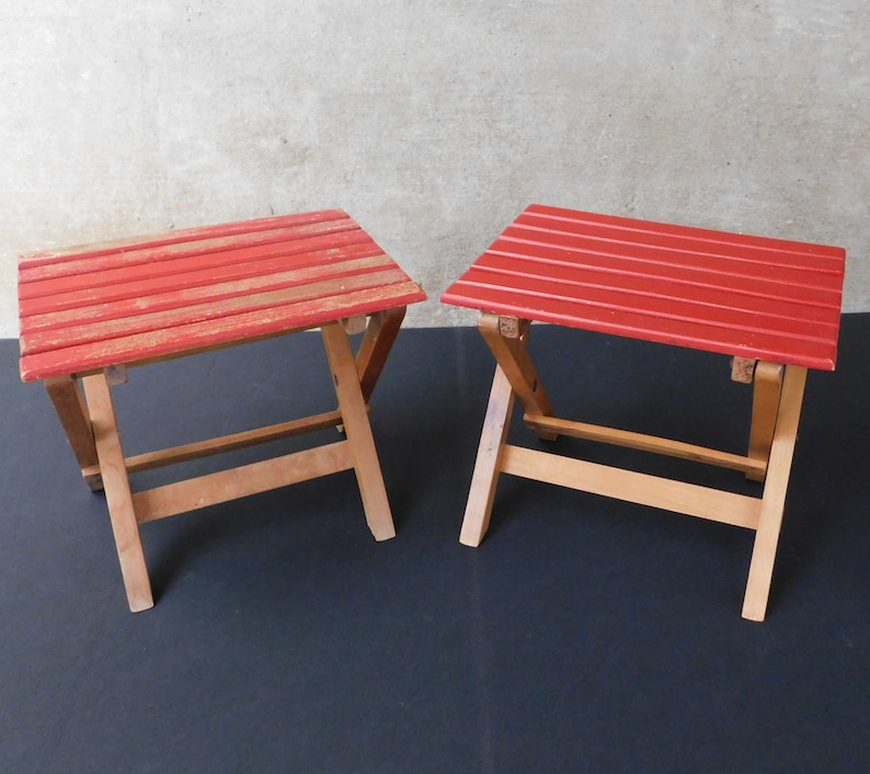 May include: Two red folding stools with wooden frames. The stools are made of wood and have a red painted finish.