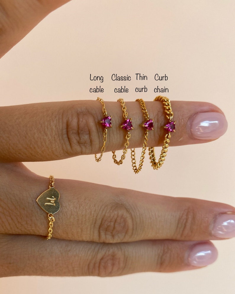 Op de afbeelding: Een verzameling goudkleurige kettingringen, elk met een uniek ontwerp. De ringen omvatten een hartvormige ring met een initiaal en ringen met roze vierkante edelstenen. De tekst in de afbeelding luidt: Long cable, Classic cable, Thin curb, Curb chain.