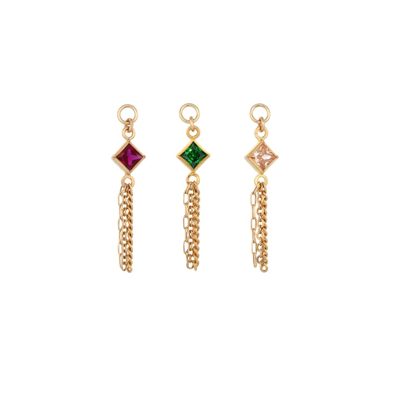 May include: Three gold-toned metal charms, each featuring a square-cut gemstone in magenta, emerald green, and pale peach. Each charm is suspended from a circular jump ring and includes a delicate dangling gold chain attached to the base.