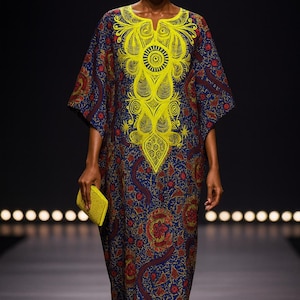 May include: A long, patterned dress in blue, red, and yellow. The dress has a yellow embroidered design on the bodice and is paired with a yellow clutch. The model is wearing yellow earrings and shoes. The dress is floor-length.