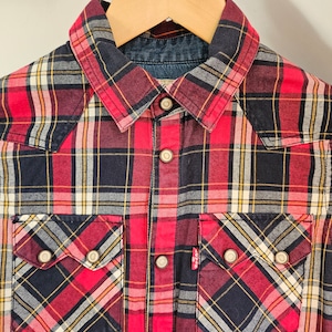 May include: Red and black plaid long-sleeve shirt with a button-down collar and two chest pockets.