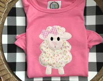 May include: Pink short-sleeved shirt with a white embroidered lamb with a pink bow and floral print. The shirt has a small label that says "BB" and "Little Button".