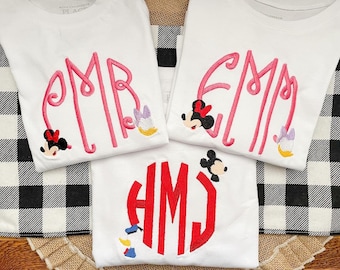 May include: Three white t-shirts with embroidered monograms and Disney characters. The monograms are "PMB", "EMM", and "HMJ". The characters are Mickey Mouse and Minnie Mouse.