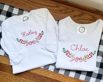 May include: Two white long-sleeved shirts with embroidered Christmas designs. The shirts are personalized with the names "Hatley" and "Chloe".