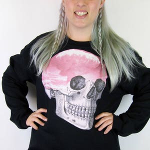 May include: Black sweatshirt with a large anatomical skull graphic printed on the front. The skull is pink and white.