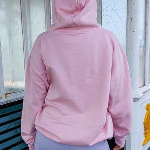 May include: A pink hoodie with a drawstring hood. The hoodie is made of a soft, comfortable material and has a relaxed fit.