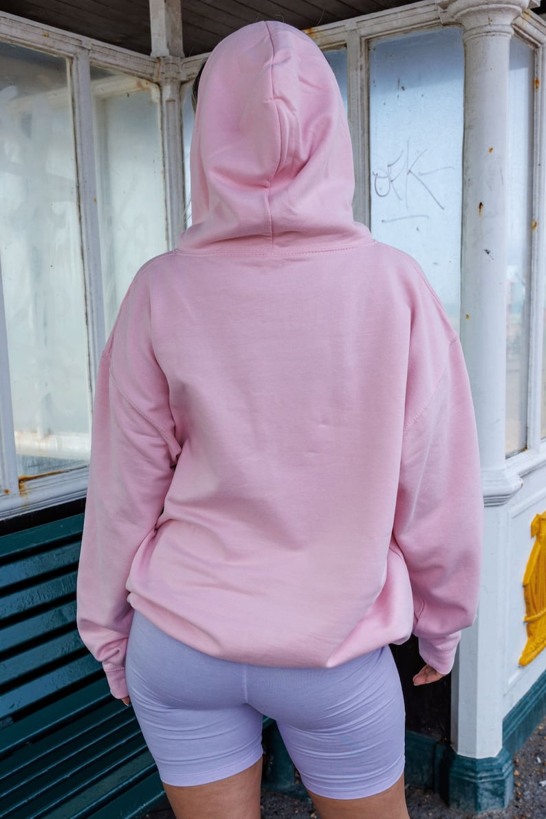 May include: A pink hoodie with a drawstring hood. The hoodie is made of a soft, comfortable material and has a relaxed fit.