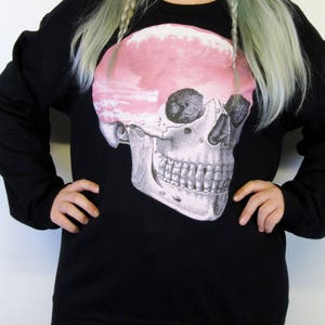 May include: Black sweatshirt featuring a graphic print of a skull with a pink cloud inside. The skull is labelled with numbers.