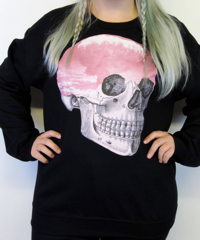 May include: Black sweatshirt featuring a graphic print of a skull with a pink cloud inside. The skull is labelled with numbers.