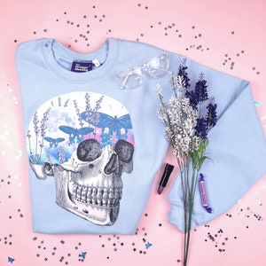 Pu&ograve; includere: Felpa blu chiaro con una stampa grafica di uno scheletro con lavanda e farfalle. Il testo "The Grunge Monkey" &egrave; sull'etichetta.