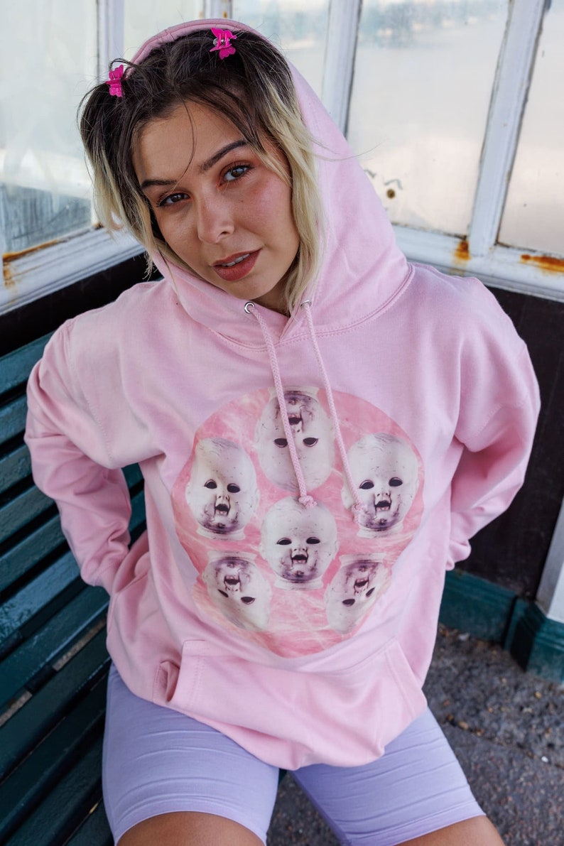 May include: A pink hoodie with a graphic print of multiple baby faces in a circle on a pink background.