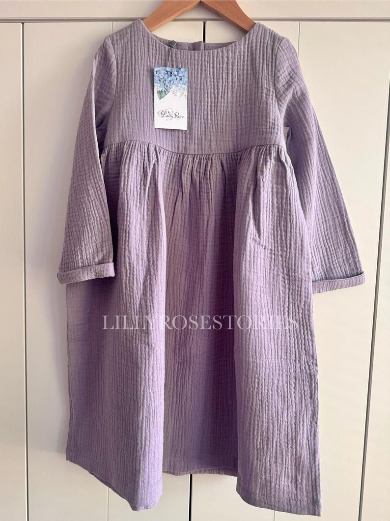 K&ouml;nnte beinhalten: Ein lang&auml;rmeliges, lavendelfarbenes Kleid mit einem gerafften Rock und einem runden Ausschnitt. Das Kleid ist aus einem weichen, strukturierten Stoff gefertigt und hat eine lockere Passform.