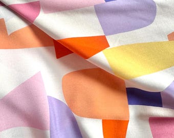 May include: White fabric with a colorful geometric pattern. The design features abstract shapes in shades of orange, pink, purple, and yellow. The fabric is folded, creating shadows and texture.