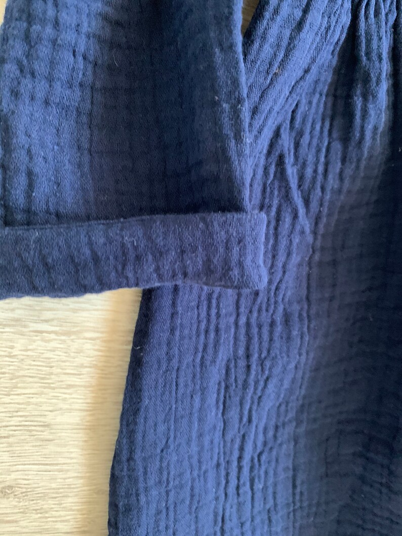 K&ouml;nnte beinhalten: Nahaufnahme eines dunkelblauen Baumwollkleidungsst&uuml;cks mit einer strukturierten Oberfl&auml;che. Der Stoff hat ein leicht zerknittertes Aussehen.
