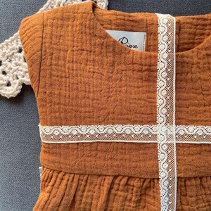 K&ouml;nnte beinhalten: Ein braunes, &auml;rmelloses Kleid mit wei&szlig;em Spitzenbesatz. Das Kleid hat einen R&uuml;schen-Saum und ein kleines wei&szlig;es Etikett mit dem Wort "Rose" darauf.