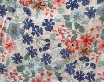 May include: Close-up of a fabric with a floral pattern. The design features a dense arrangement of small flowers in shades of red, blue, and light blue, set against a white background. Green leaves and small red berries are also present.