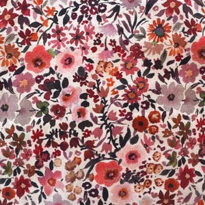 May include: A close-up of a floral fabric with a dense pattern of small flowers in shades of red, pink, orange, and purple. The flowers are set against a cream-colored background, creating a vibrant and detailed textile design.