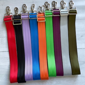 May include: Ten different colored adjustable straps with silver hardware. The straps are made of a woven material and are available in red, black, lavender, blue, orange, green, purple, gray, and olive green.