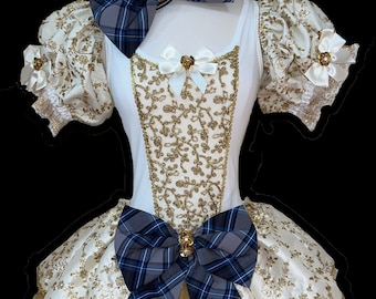 May include: A white and gold tulle dress with a blue and gray plaid bow. The dress has a white bodice with gold embroidery and puff sleeves. The skirt is layered with tulle and has a gold trim.