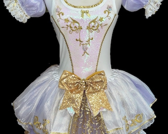 May include: A white and lavender tulle tutu with gold embroidery and a gold sequin bow. The tutu has a white bodice with a lavender overlay and gold trim.