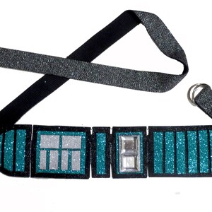 May include: A teal and black glitter belt with a silver buckle and a black strap. The belt is made of fabric and has a sparkly finish.