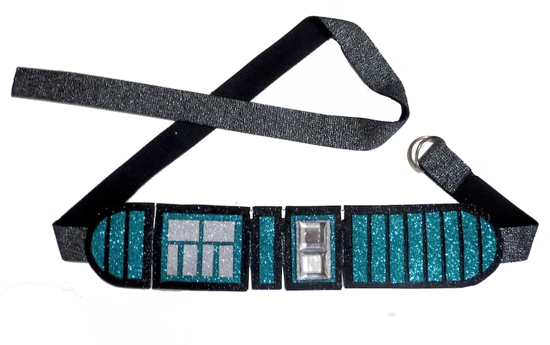 May include: A teal and black glitter belt with a silver buckle and a black strap. The belt is made of fabric and has a sparkly finish.