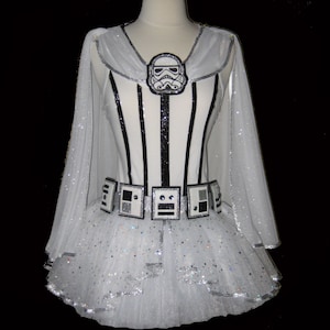 May include: White tutu with a black and white striped bodice and a silver glitter cape. The bodice features a black and white Stormtrooper helmet graphic. The tutu has a silver glitter trim and a black and white belt with silver buckle.