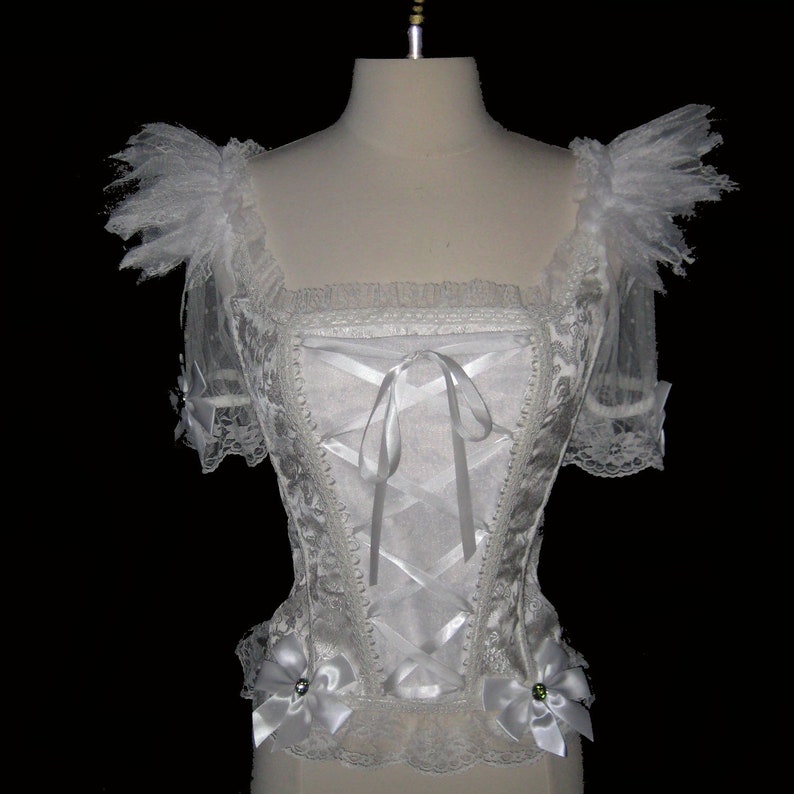 May include: White lace corset top with a satin ribbon tie and lace trim. The top has short sleeves with lace ruffles and is decorated with white satin bows.