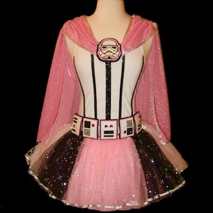 May include: Pink and black tutu with a white and black striped bodice and a pink cape. The bodice has a white stormtrooper helmet appliqué. The tutu has black and silver glitter.