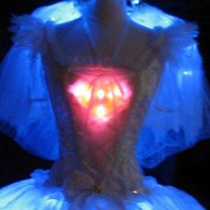 May include: A white bridal gown with a red light-up heart design on the bodice. The gown is illuminated with blue lights.