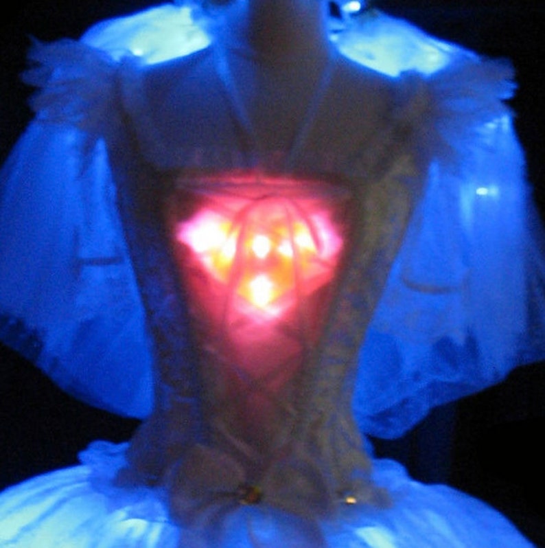 May include: A white bridal gown with a red light-up heart design on the bodice. The gown is illuminated with blue lights.