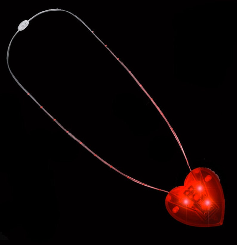 May include: A red heart-shaped LED light necklace with a clear plastic cord. The necklace is lit up and the heart is glowing.