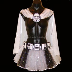 May include: A white tutu with black glitter and a black and white belt with a Stormtrooper helmet design. The tutu is worn by a mannequin with a white cape.