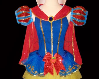 May include: A blue and red Snow White costume with a white collar, gold trim, and a red bow with an apple design. The costume includes a tulle skirt and a cape.