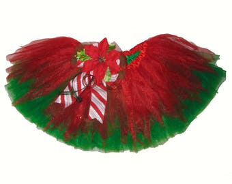 May include: Red and green tulle tutu with a poinsettia flower and candy cane ribbon. The tutu is perfect for a Christmas party or holiday event.