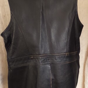 May include: Black leather vest with a notched collar and a tailored fit. The vest features a horizontal seam across the back and vertical seams down the sides. The vest is sleeveless and has a classic, timeless design.