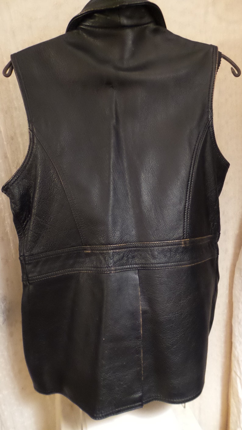 May include: Black leather vest with a notched collar and a tailored fit. The vest features a horizontal seam across the back and vertical seams down the sides. The vest is sleeveless and has a classic, timeless design.