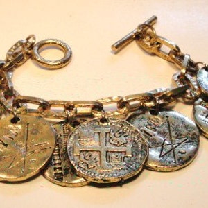 May include: A gold chain bracelet with multiple charms, each featuring a different design. The charms are round and have a worn, antique look. The bracelet has a toggle clasp.