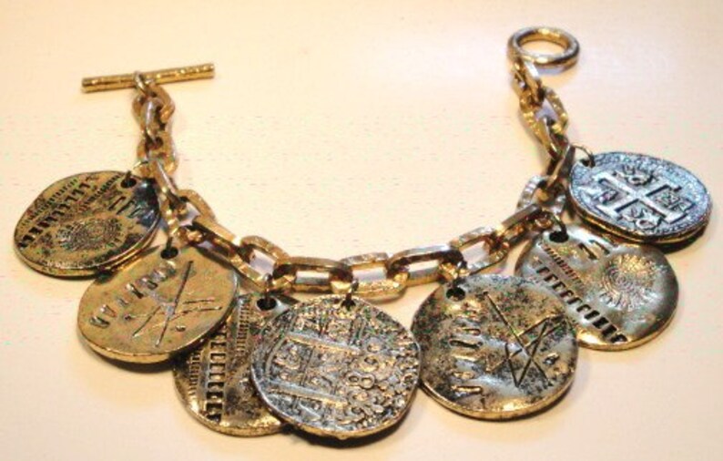 May include: A gold chain bracelet with multiple round charms, each featuring a different design. The charms are made of a combination of gold and silver metal and have intricate details.