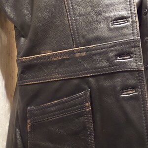 May include: Black leather vest with a tailored fit. Features include a notched lapel, button closure, and a single pocket. The vest has visible stitching and a belt detail at the waist. The leather shows signs of wear.