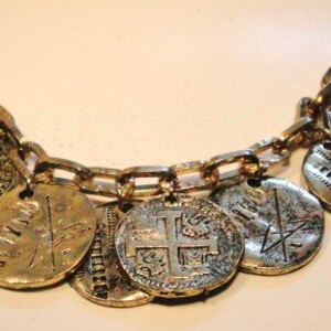 May include: A gold bracelet with a chain and multiple coin-shaped charms. The charms have different designs, including a cross, a sword, and a shield.