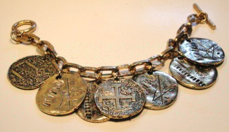 May include: A gold bracelet with a chain and multiple coin-shaped charms. The charms have different designs, including a cross, a sword, and a shield.