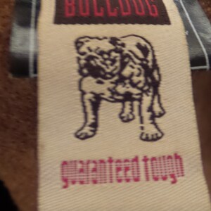 May include: Close-up of a tag with the word "BULLDOG" in red letters on a brown background. Below the word is an illustration of a bulldog. The words "guaranteed tough" are printed in pink.