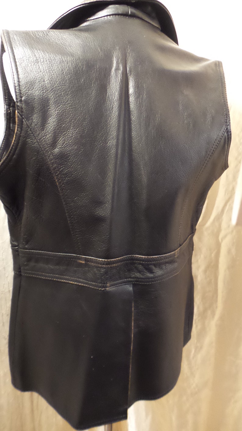 May include: A black leather vest with a collar and a tailored fit. The vest has a classic design with visible stitching and a belt detail at the waist. The leather appears to be slightly worn, adding character to the garment.