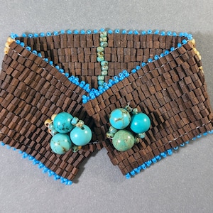 Könnte beinhalten: Ein braunes Perlenarmband mit türkisfarbenen Steinen. Das Armband besteht aus kleinen Holzquadraten und hat einen blauen Rand.