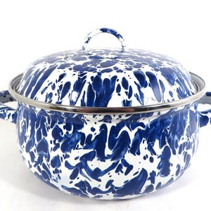 May include: A round enamel pot with a lid, featuring a blue and white marbled splatter pattern. The pot has two side handles and a metal rim around the top edge and the lid. The lid includes a small arched handle on the top center for lifting.